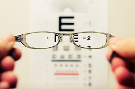Selective focus of eye glasses being held in front of eye chart